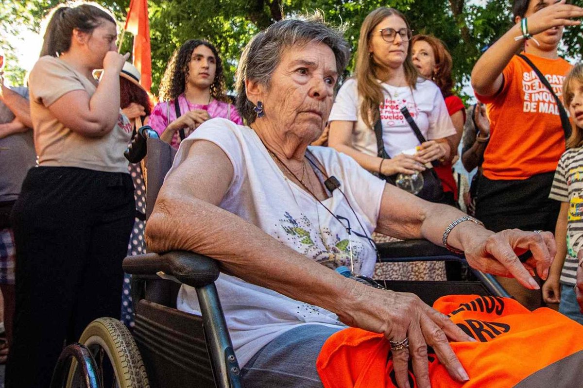 Tekerlekli sandalyede oturan yaşlı bir kadın ve çevresinde duran kalabalık