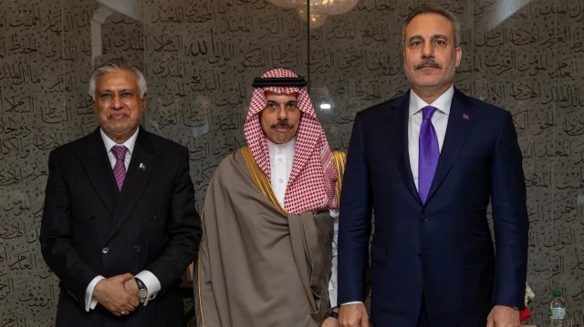Arapça yazılarla kaplı bir duvarın önünde yan yana poz veren üç kişi